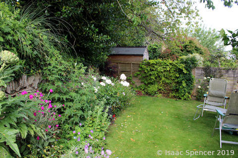view of back garden, garden chairs on grass and a flower border on the left side